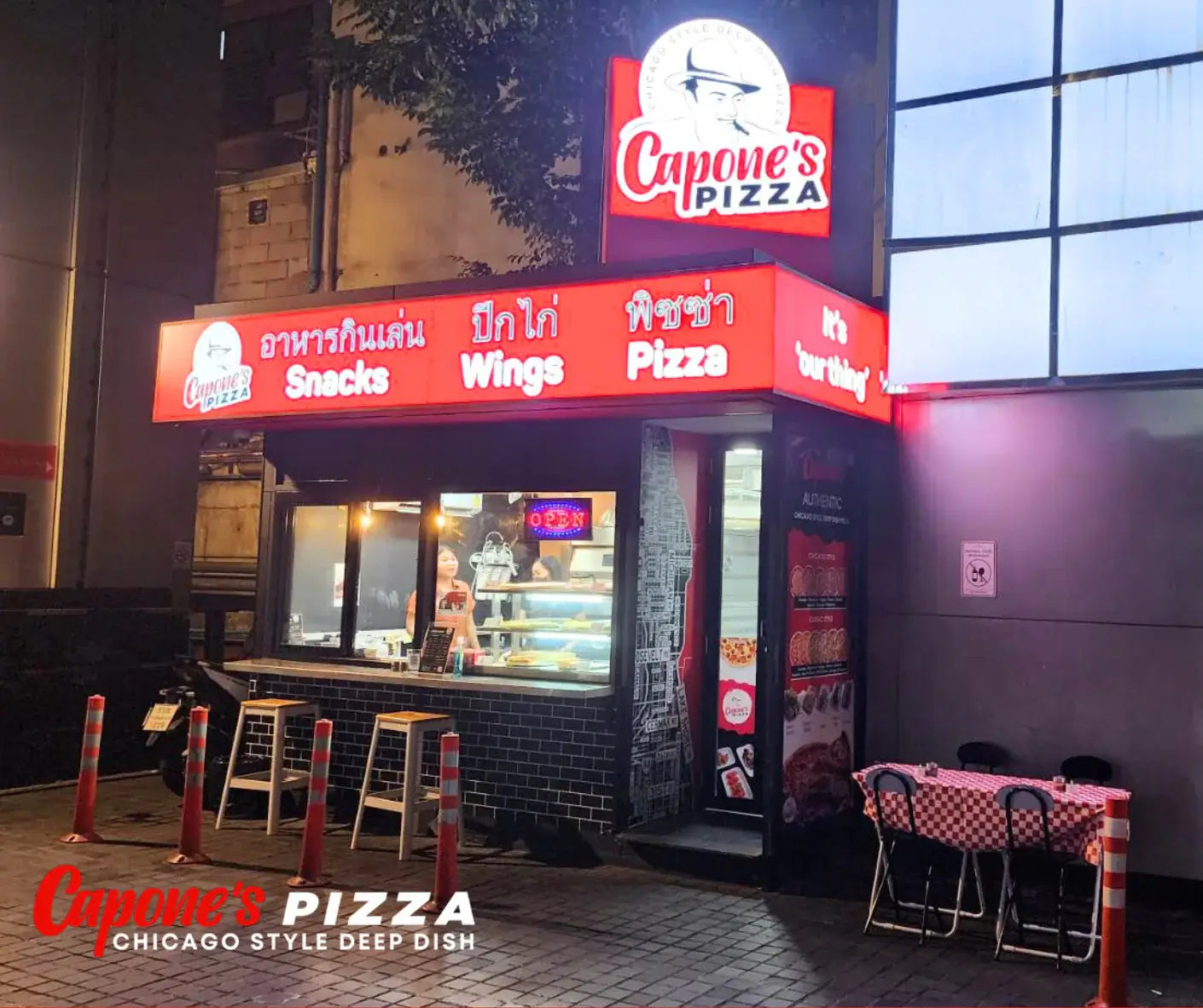 Capone's Pizza restaurant exterior with neon sign and outdoor seating area.